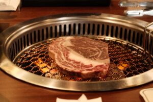 Close-up of marbled beef steak grilling on a Korean barbecue, showcasing its texture.